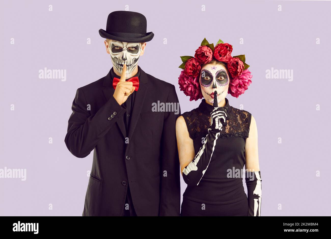Couple in Halloween costumes put fingers to lips asking you to be silent and keep secret Stock Photo
