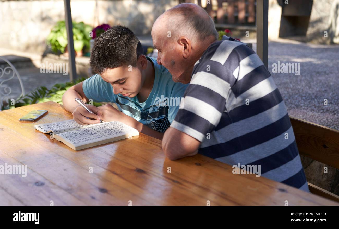 A elderly man sitting doing crosswords hobby with his grandson. Stock Photo