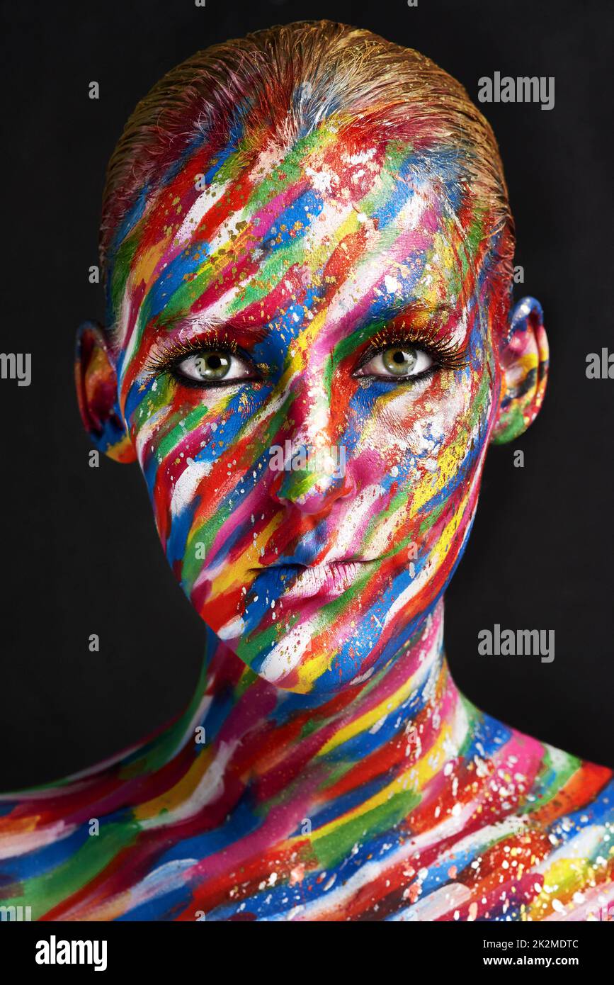 There's nothing dull about beauty. Studio shot of a young woman posing with brightly colored paint on her face against a black background. Stock Photo