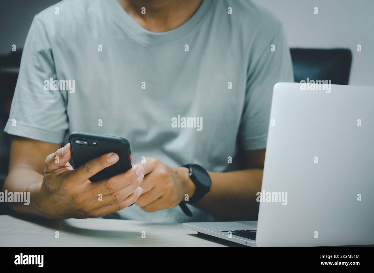 man hand holding smartphone and computer laptop to working technology searching internet, sending sms, using text messenger or online banking. Stock Photo