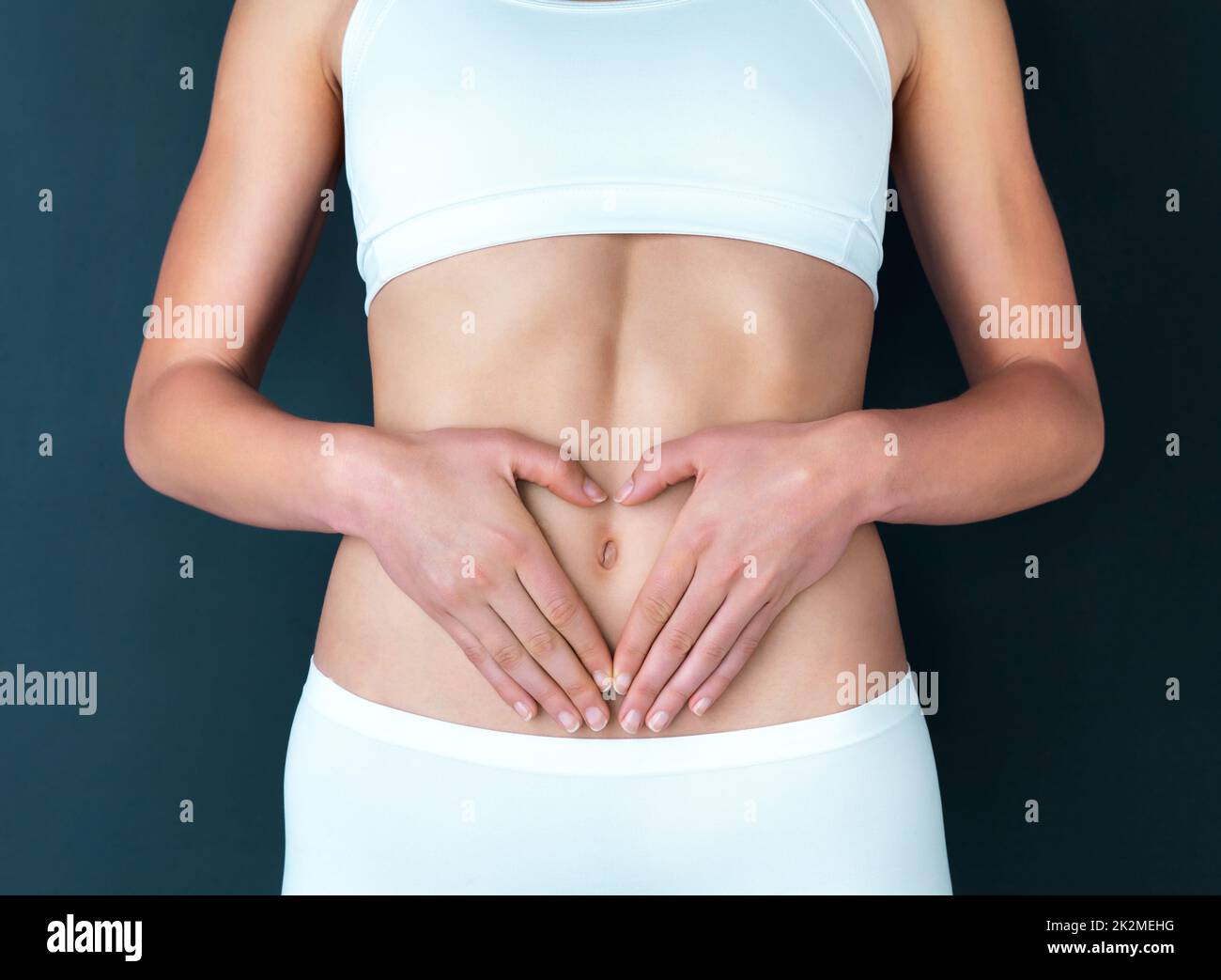 For the greatest wealth, invest in your health. Studio shot of a fit young woman making a heart shaped gesture over her stomach against a dark background. Stock Photo