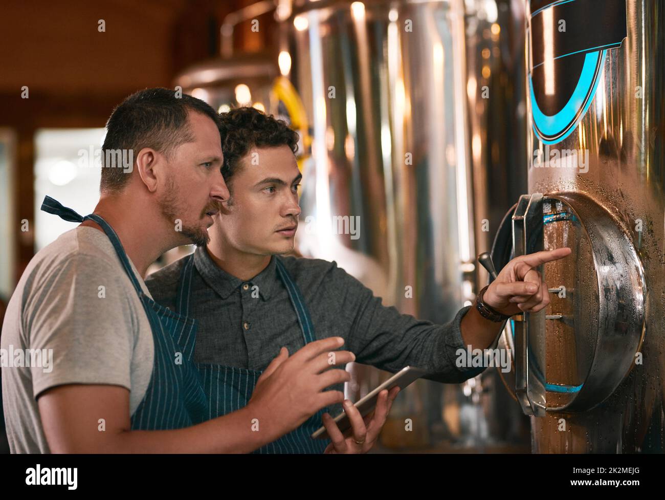 Is this container cold enough. Shot of two young working men doing inspection of their beer making machinery inside of a beer brewery during the day. Stock Photo