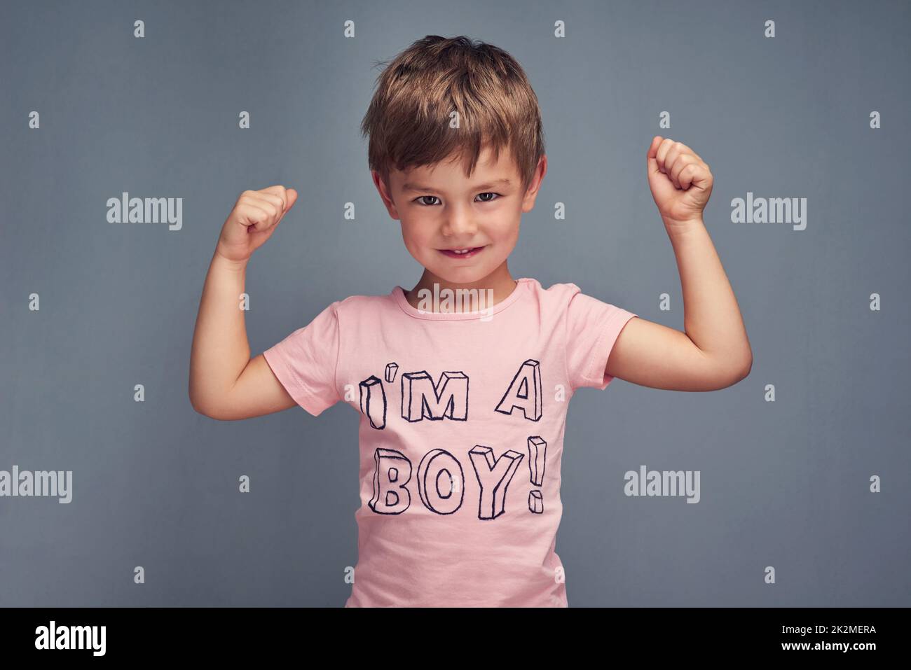 Tough guys wear pink. Studio portrait of a cheering boy wearing a shirt with Im a boy printed on it against a gray background. Stock Photo