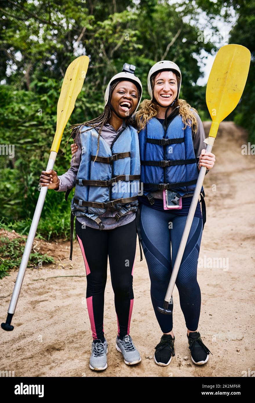 We are ready to go rafting again. Portrait of two cheerful young women wearing protective gear while holding a rowing paddle outside during the day. Stock Photo