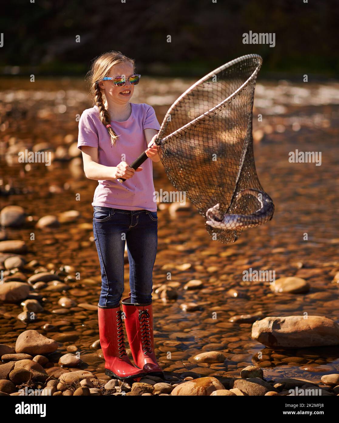 I got one. Shot of a young girl holding a fishing net with a fish in it. Stock Photo
