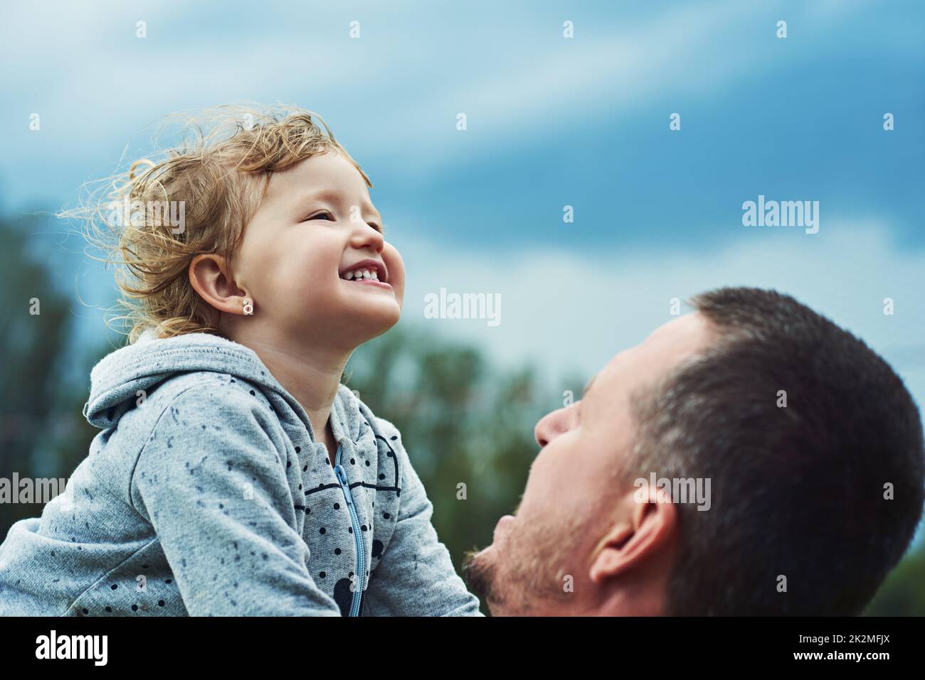 Happy as can be. Shot of a cheerful little girl being picked up by her father outside during a cloudy day. Stock Photo