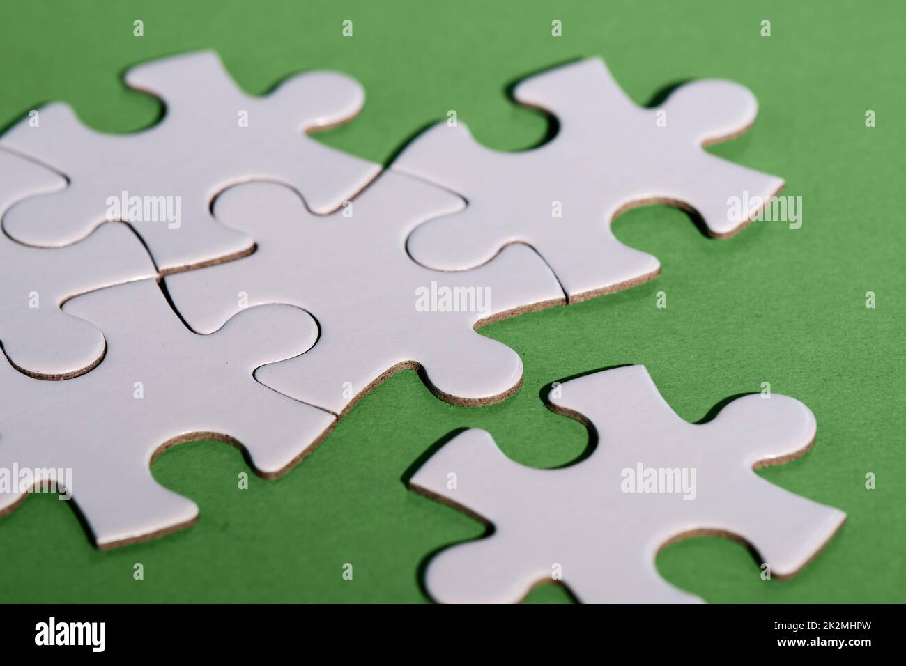 Close-up on jigsaw puzzle pieces, blank white paper jigsaw puzzle elements linked together and separate. Closeup shot on green paper. Stock Photo
