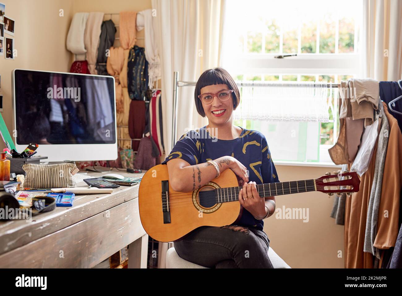 She has music in her soul. Portrait of a stylish young woman sitting in her eclectic toom playing a guitar. Stock Photo