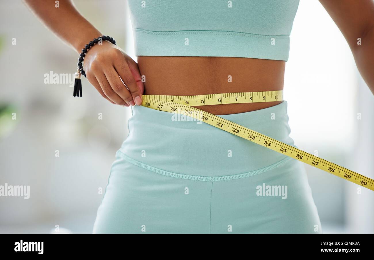 A few more inches and Id have reached my goal. Cropped shot of an unrecognisable woman standing alone and using a measuring tape around her waist in a yoga studio. Stock Photo