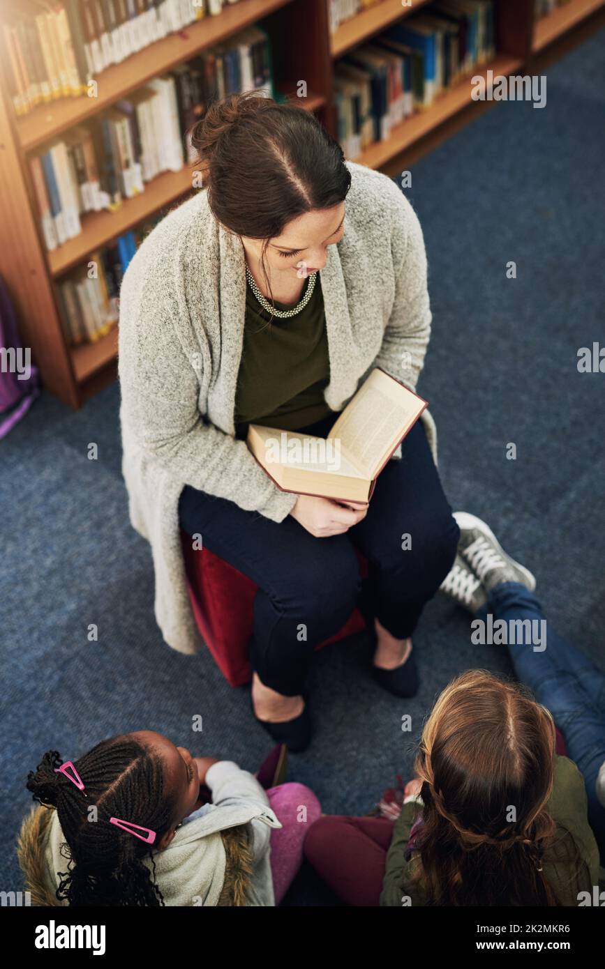 Everyone loves a good story. High angle shot of a teacher reading to a group of elementary school kids in the library. Stock Photo