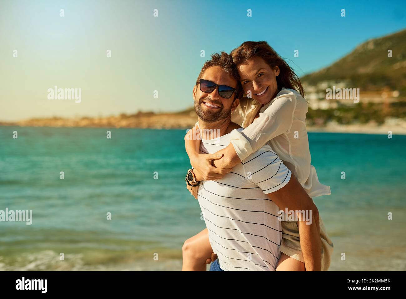The perfect day for some fun and romance. Shot of a happy young couple enjoying a piggyback ride at the beach. Stock Photo