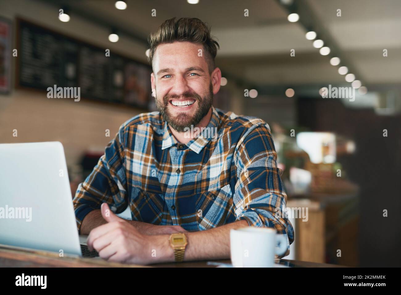 I like my internet connection as strong as my coffee. Portrait of a young man using his laptop while sitting by the window in a cafe. Stock Photo