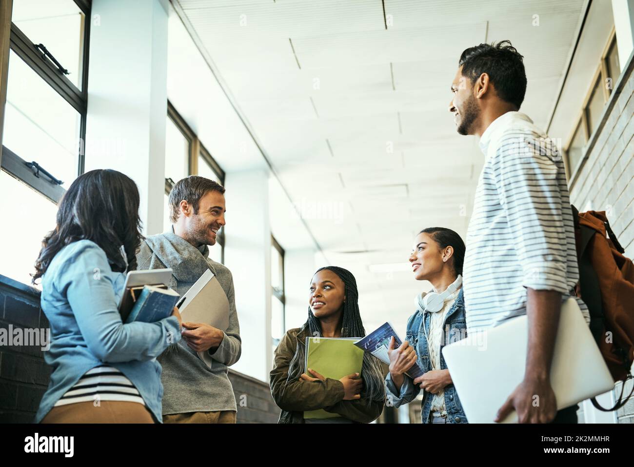 Catching up between classes. Low angle shot of a group of university students talking while standing in a campus corridor. Stock Photo