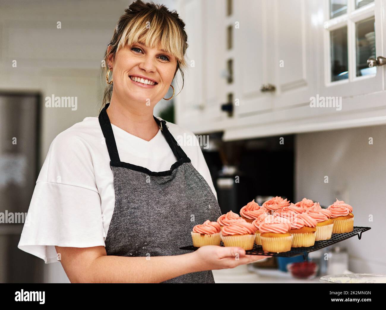 Bake yourself happy. Cropped shot of a woman holding freshly baked cupcakes in her kitchen at home. Stock Photo