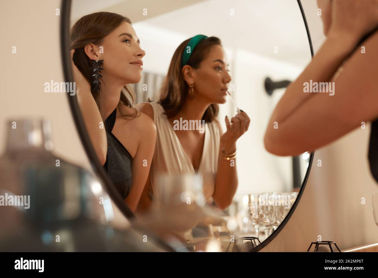 Got to keep the slay intact. Shot of two young friends standing together and using a mirror to touch up their makeup at a dinner party. Stock Photo