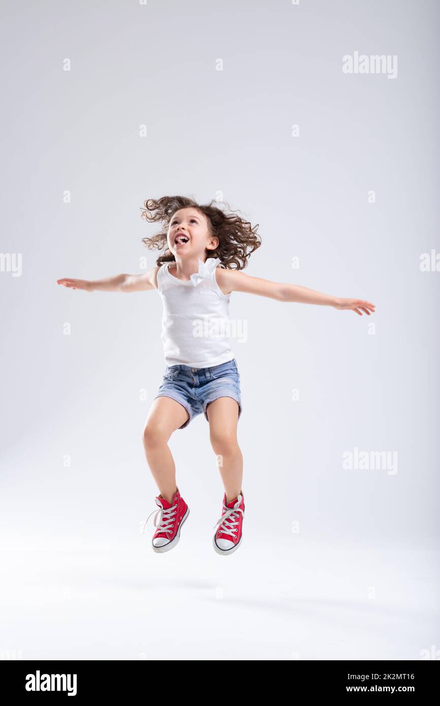 Joyful Energetic Active Little Girl In Denim Shorts And Red Sneakers 