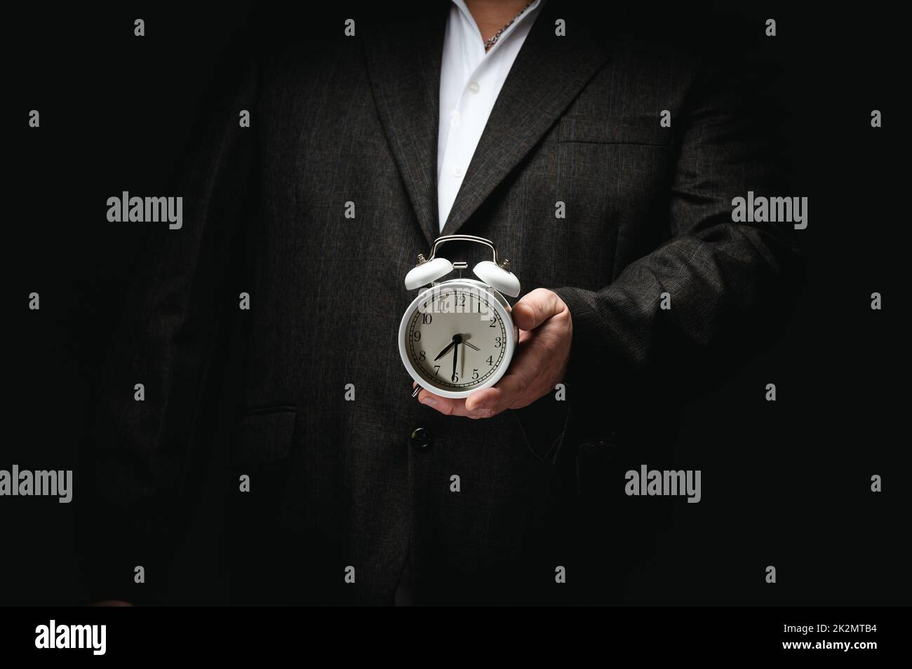 businessman in a suit holding a round alarm clock, half past seven in the morning. Clock change, early rise Stock Photo