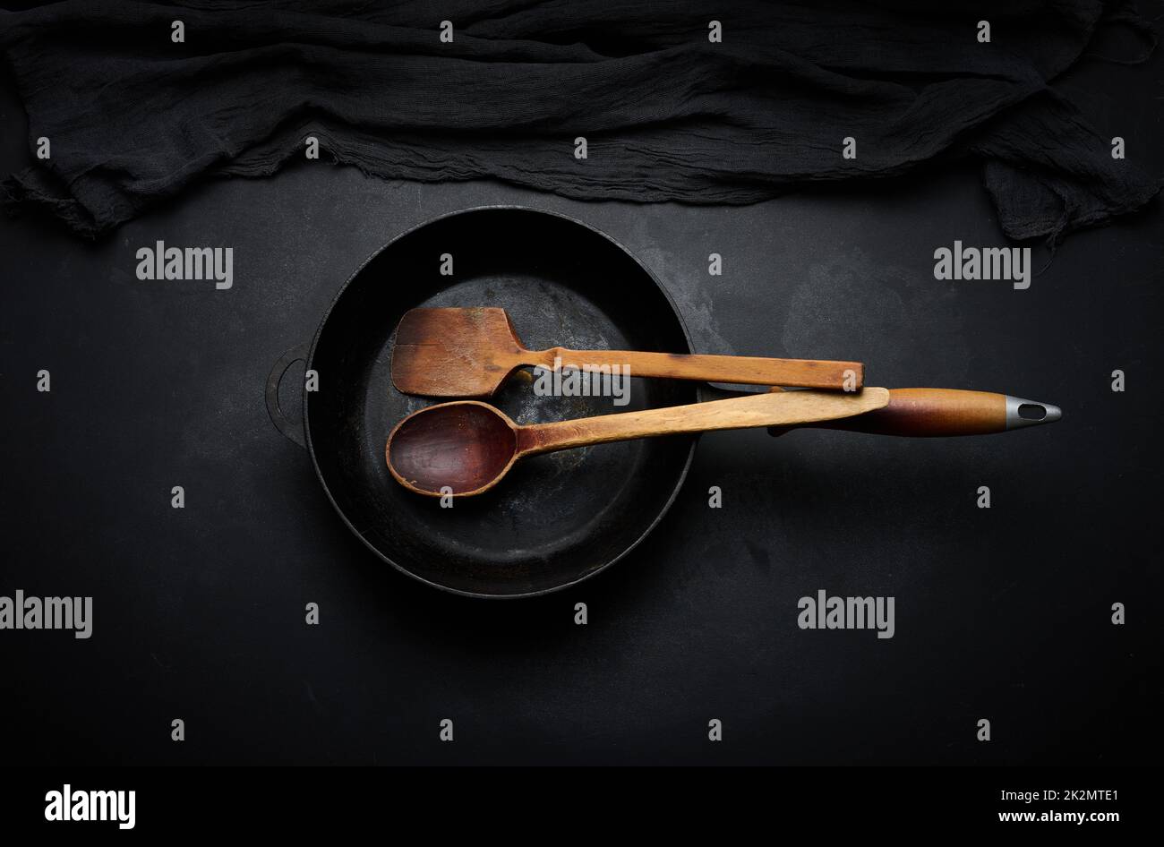 Empty round cast iron frying pan with wooden handle on black table, top