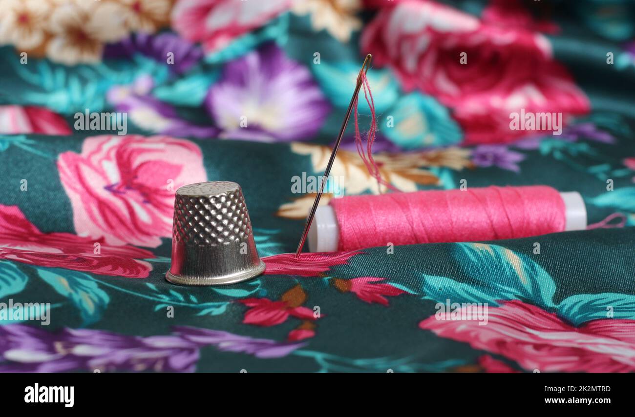 Thimble With Needle and Pink Thread on Vintage Floral Satin Fabric Stock Photo