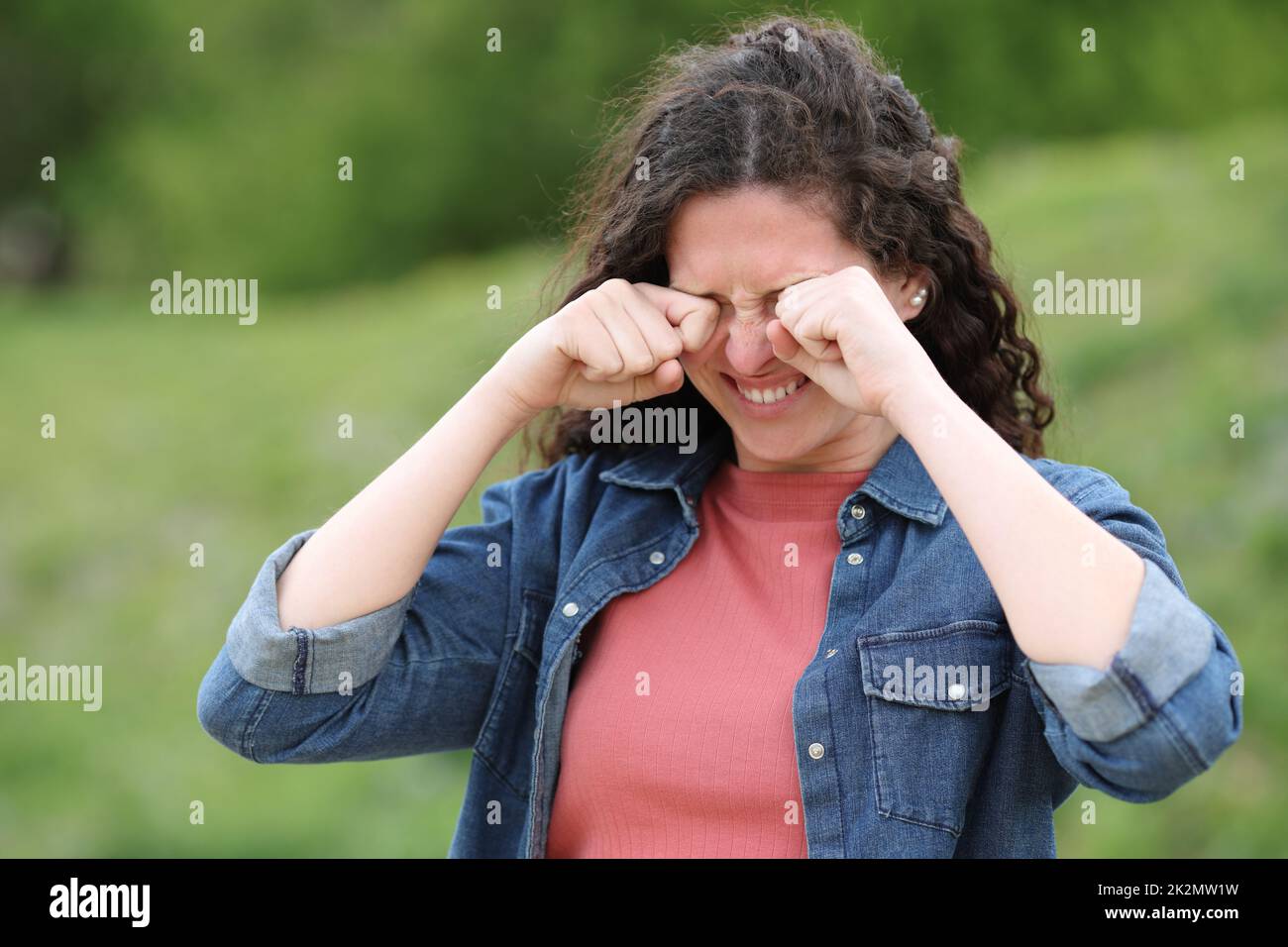 Woman scratching itchy eyes in a green park Stock Photo