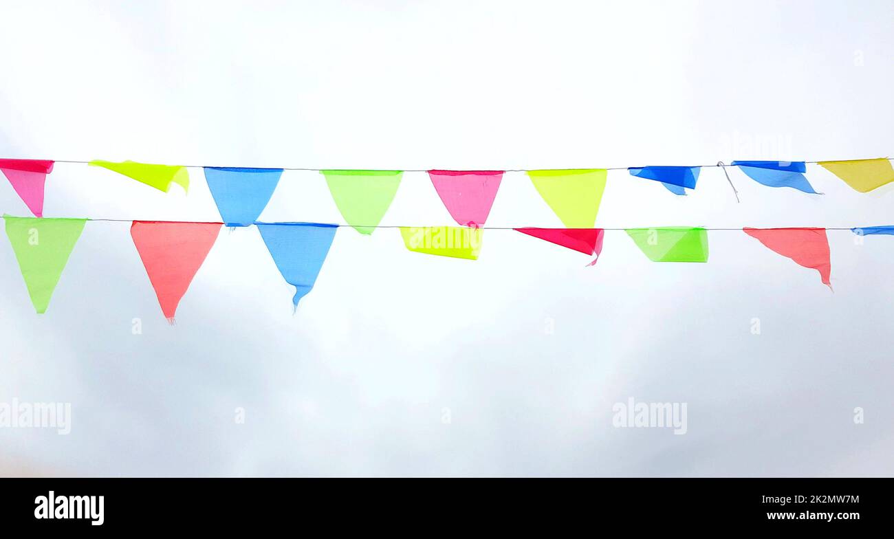 Multicolored triangular flags hang on a string and flutter in the wind against a cloudy cloudy sky Stock Photo