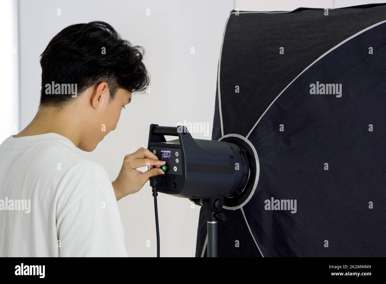 Asian photographer adjusting the brightness of lights for shooting fashion model in the studio. Stock Photo