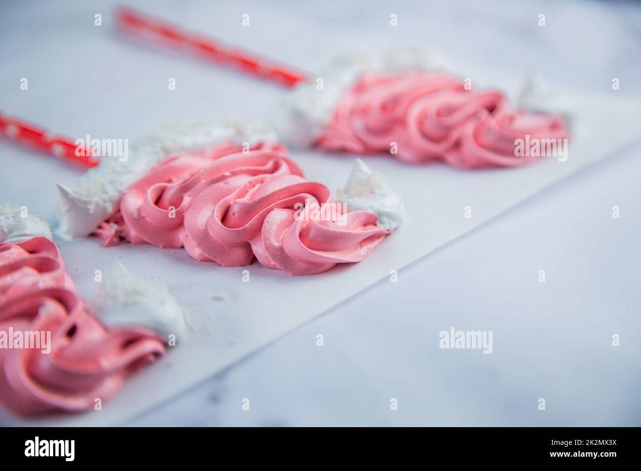 Meringue in the form of pink Christmas hats, with a white bumbone and rim lies on white parchment Stock Photo