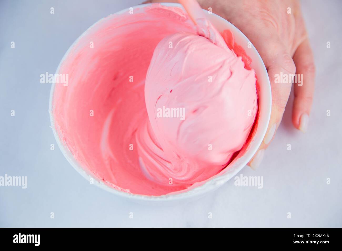 Pink confectionary meringue marengo is mixed in a white bowl on a white marble background by the hands of a pastry chef Stock Photo