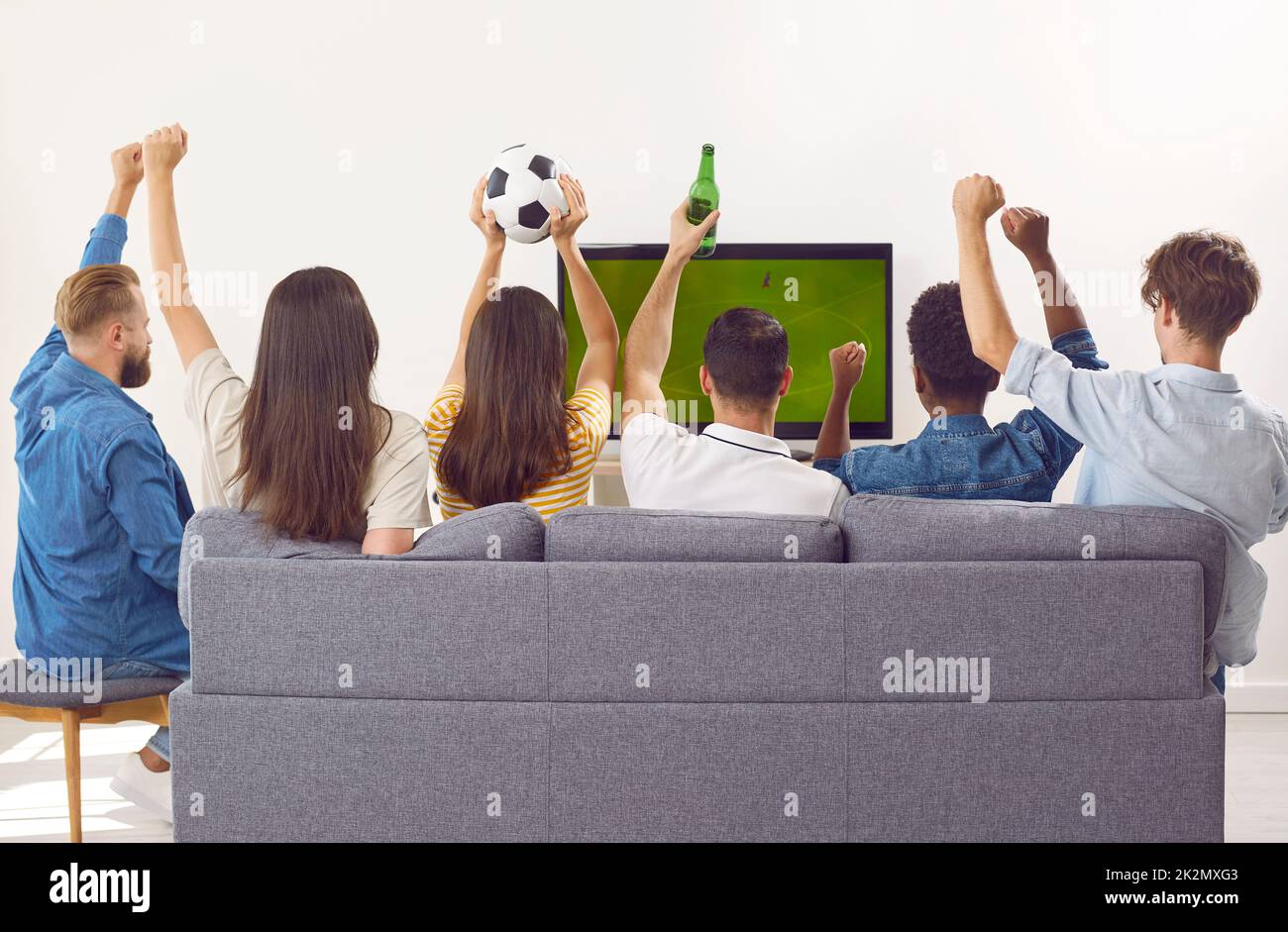 Group of happy friends sitting on couch, drinking beer and watching soccer on television Stock Photo