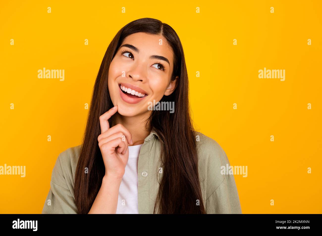 Portrait of creative minded girl toothy smile finger touch chin look empty space isolated on yellow color background Stock Photo