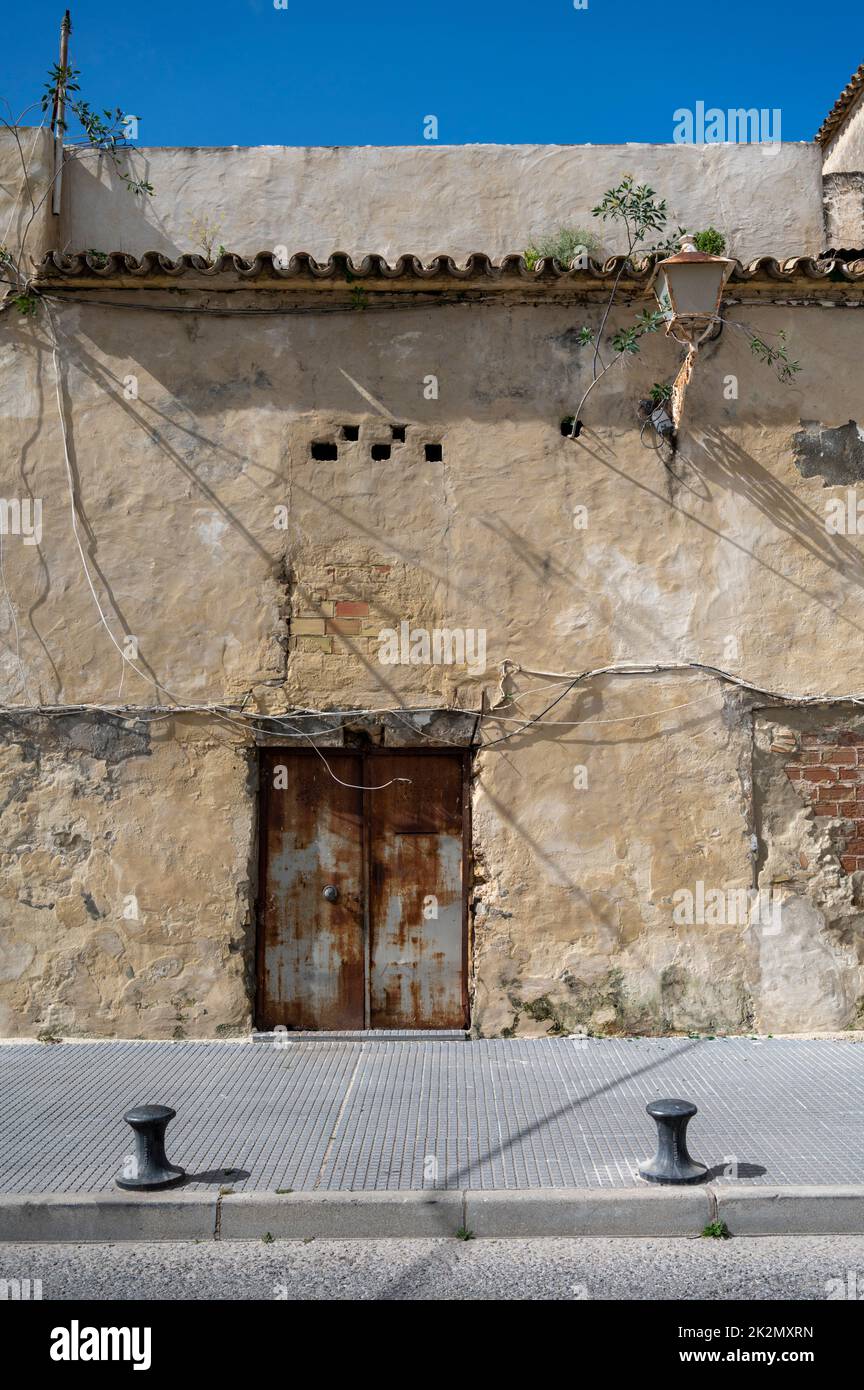 An old metal door with peeling paint on an old building with a white wall and electricity cables pinned to the wall. Stock Photo