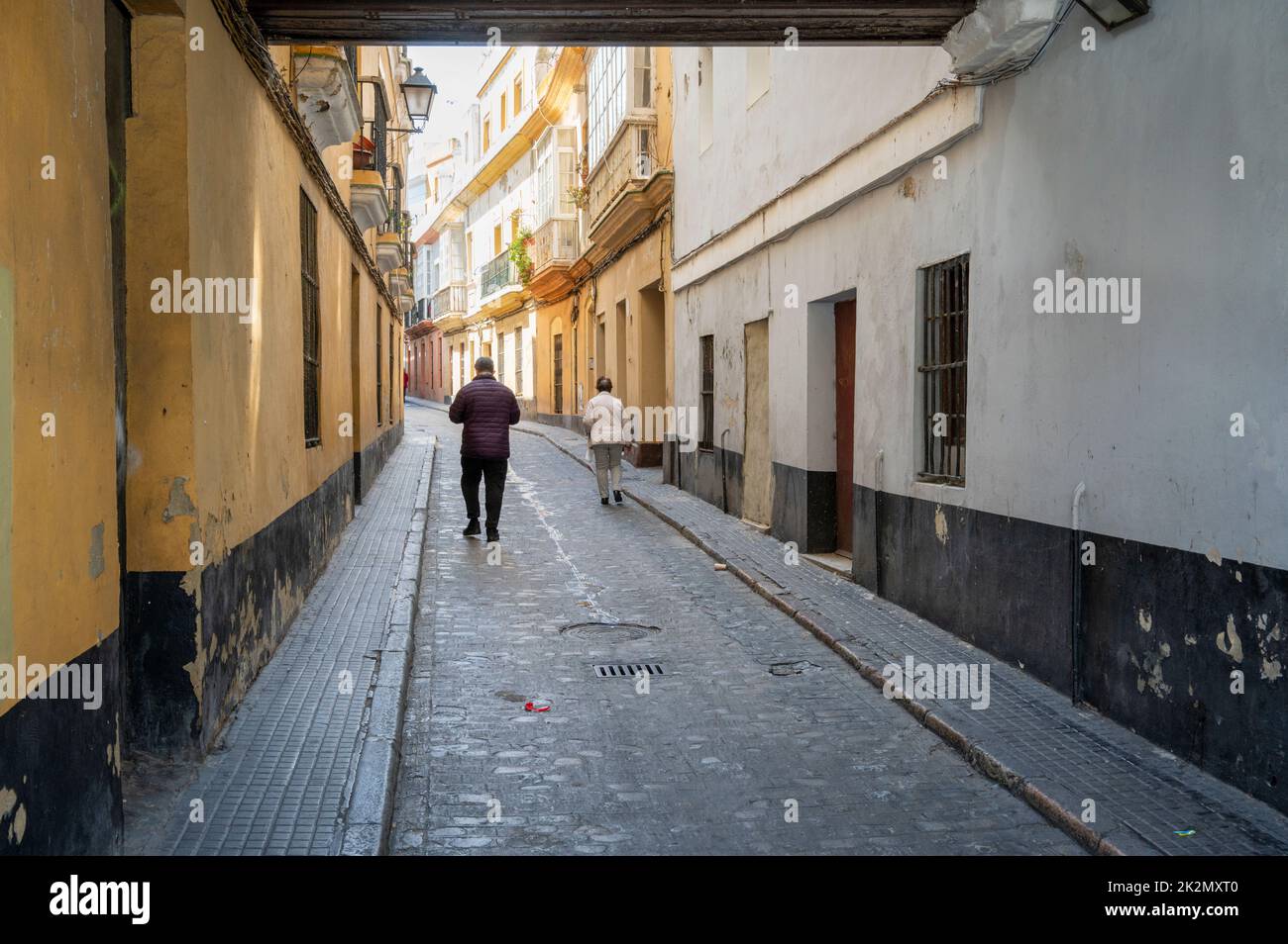 Two people walking down an old narrow street in Cadiz Spain Stock Photo