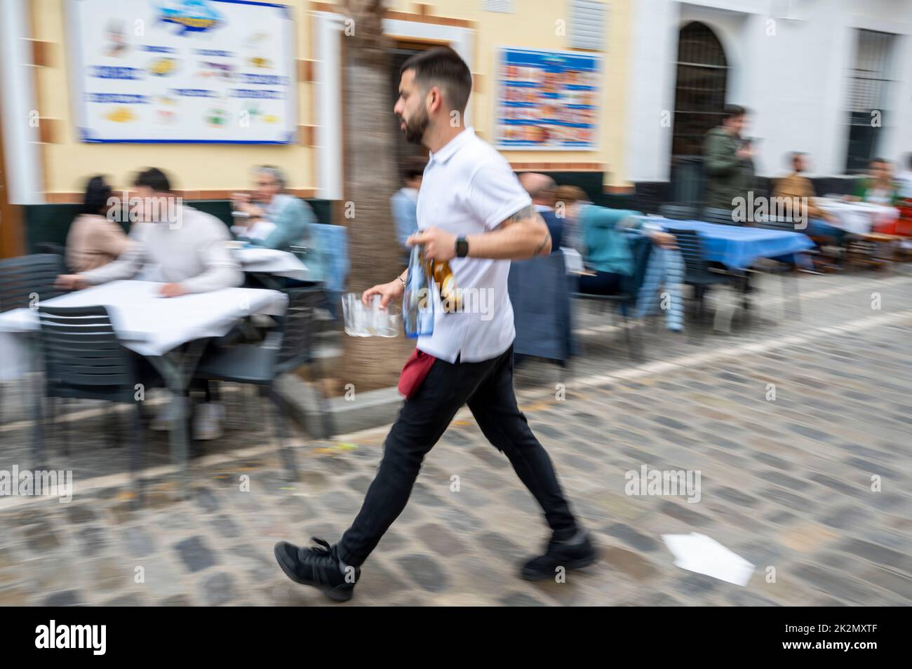 A blurred abstract image of a waiter serving tables outside in the street in Cadiz Spain with motion blur Stock Photo