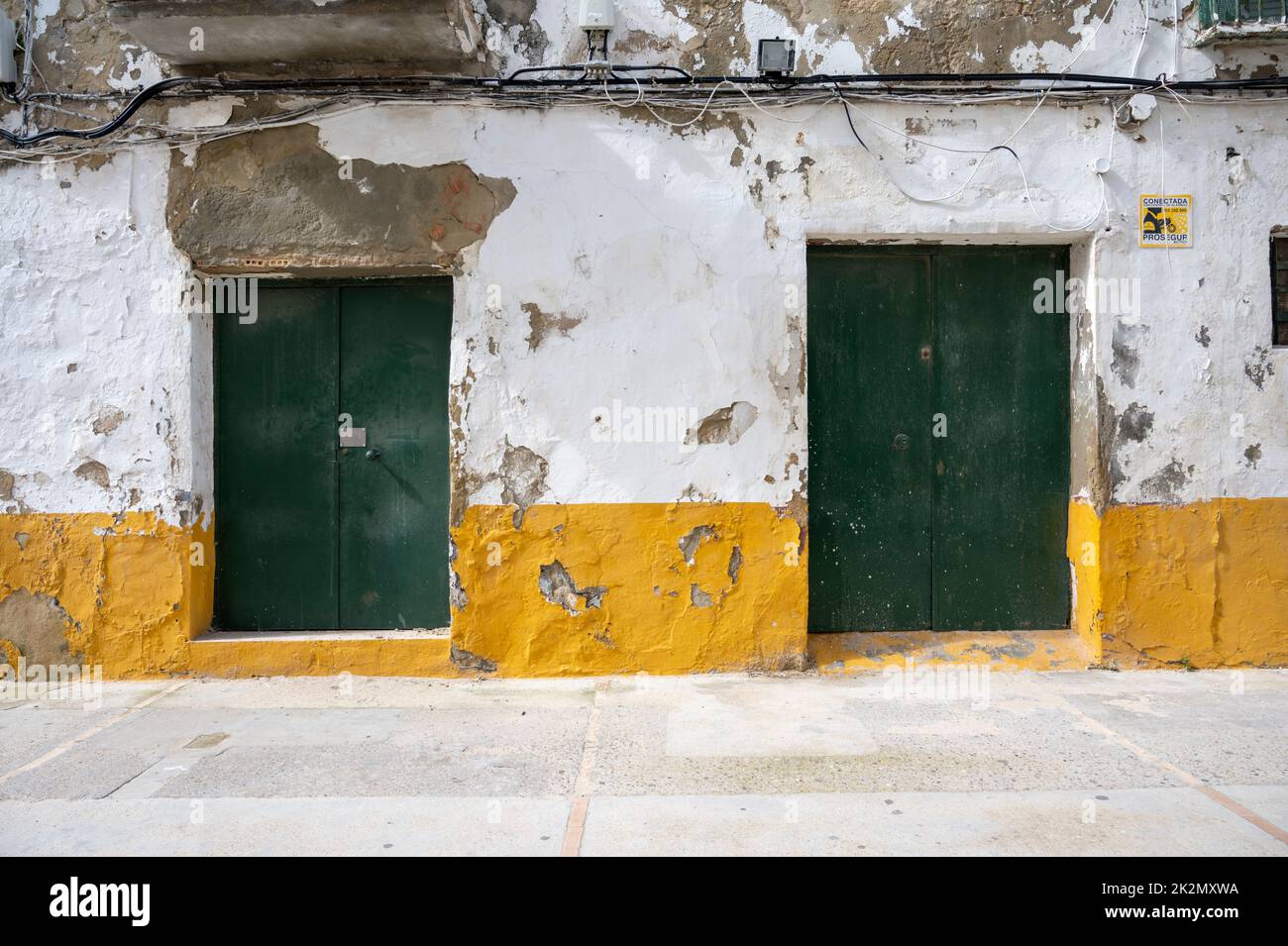 Old wooden doors painted green on a white building with yellow skirting in Spain Stock Photo