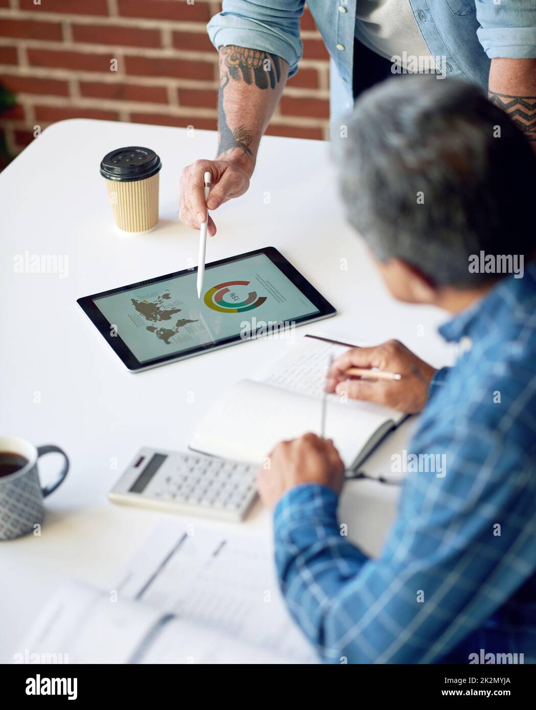two businessmen using tablet computer discussing financial graph data on mobile touchscreen device in meeting Stock Photo