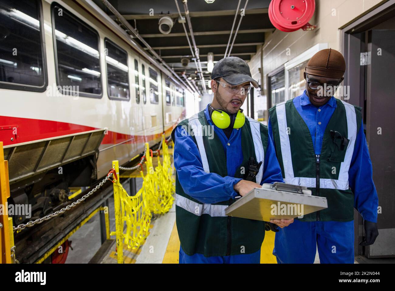 Male transit engineers with clipboard in maintenance facility Stock