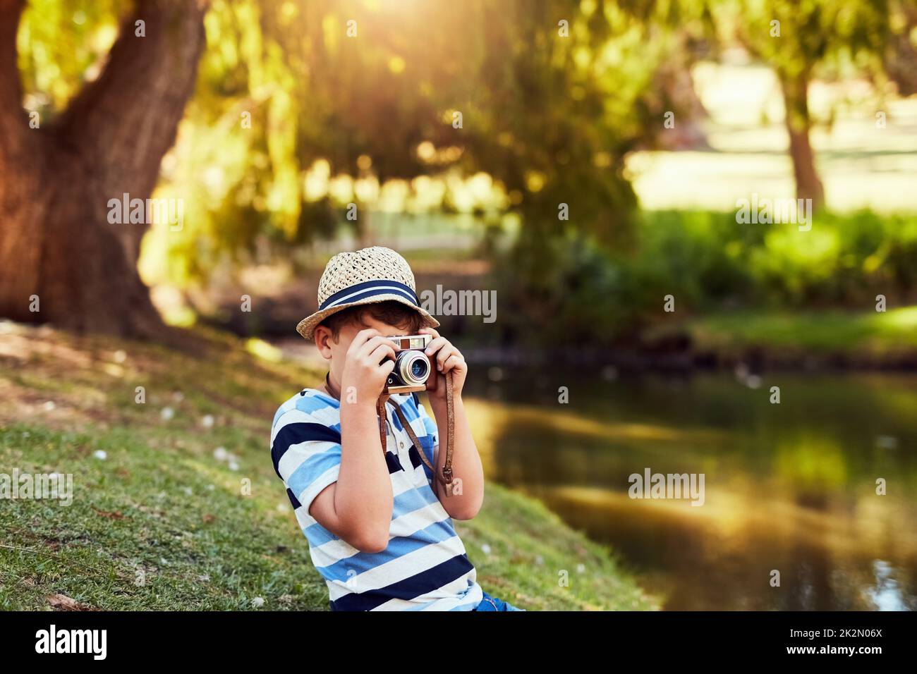 Taking some scenic shots at the park. Shot of a little boy taking a photo with a vintage camera at the park. Stock Photo
