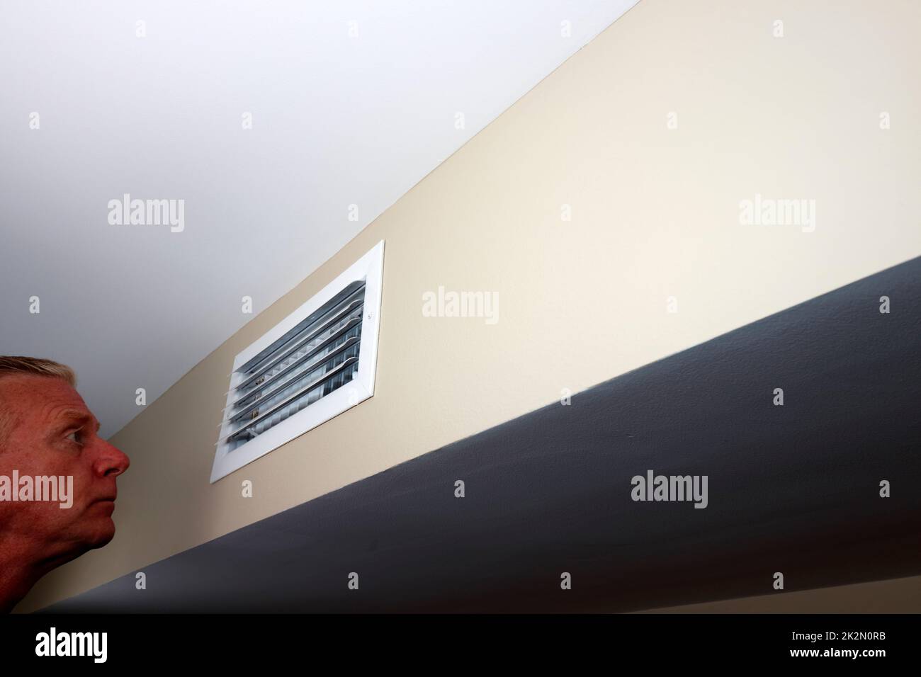 Adult Male Looking Into a Small Rectangle Air Vent on a Wall Stock Photo