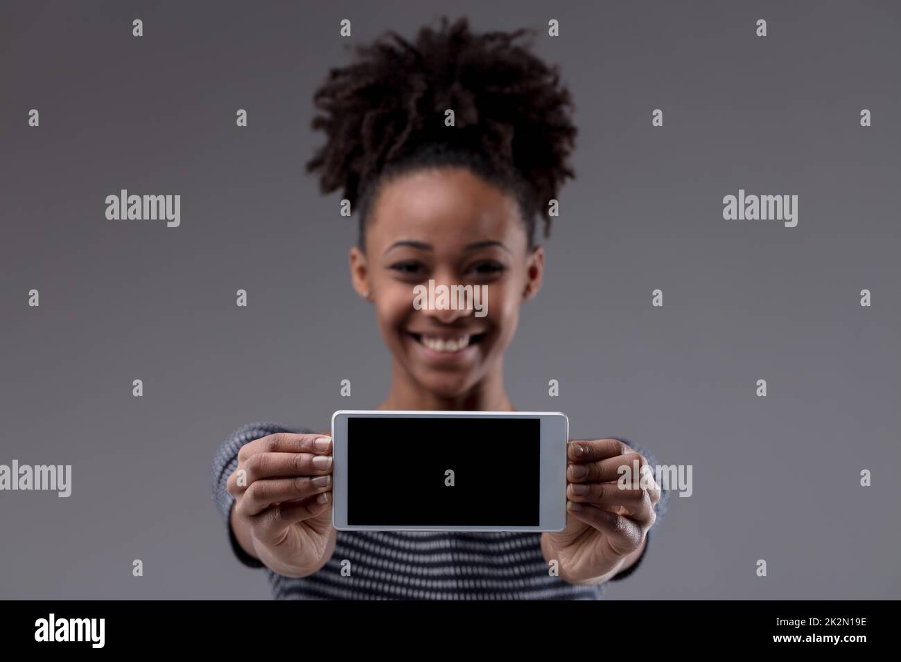 Happy excited young Black woman holding out her mobile Stock Photo