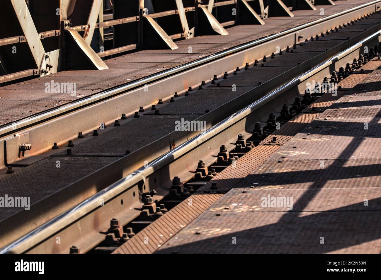 Detail of railway tracks on old metal bridge, sun casting shadows on