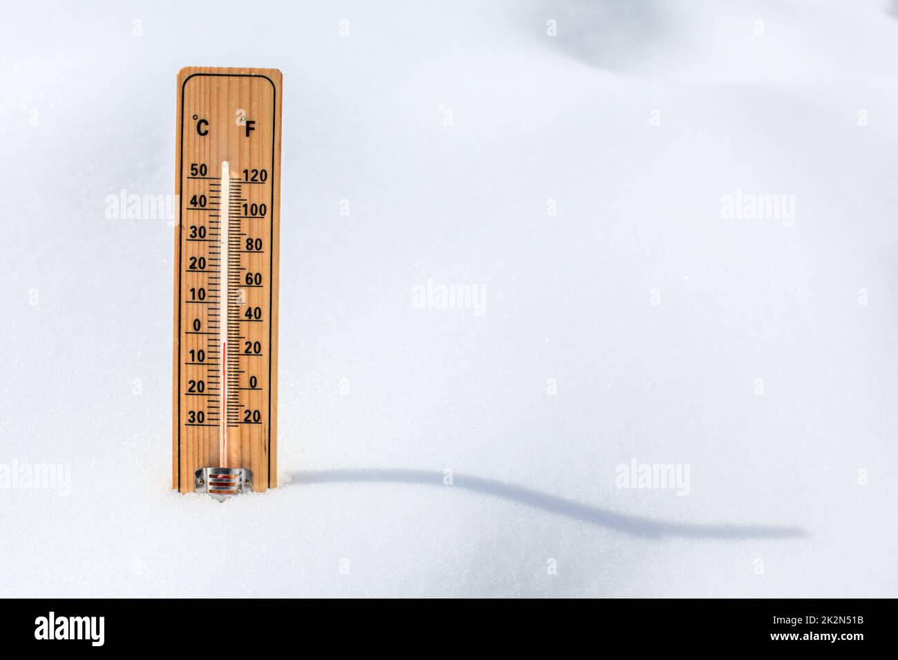 Wooden thermometer standing in snow, showing low temperature, space for