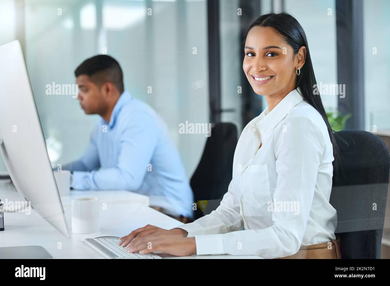 Leave the challenges to us. Shot of a young call centre agent sitting in the office with a colleague and wearing a headset. Stock Photo