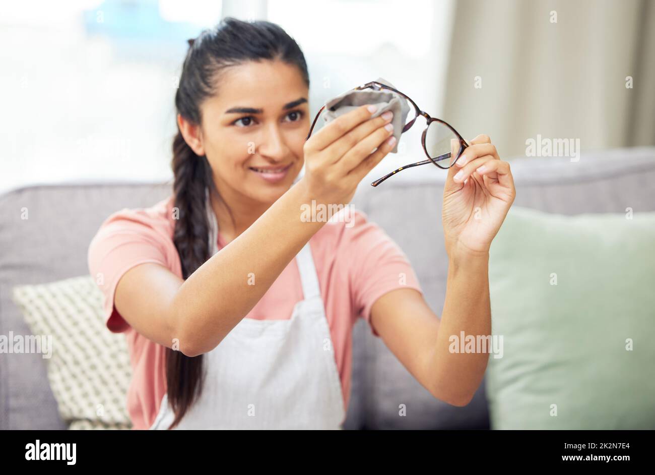 All the dirt is gone and I can see clearly again. Shot of a young woman cleaning her glasses while sitting at home. Stock Photo