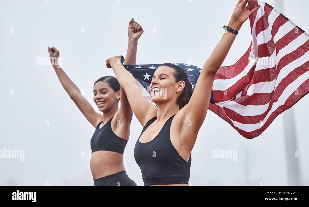 Women run the world. Shot of female athletes celebrating their win while holding a flag. Stock Photo