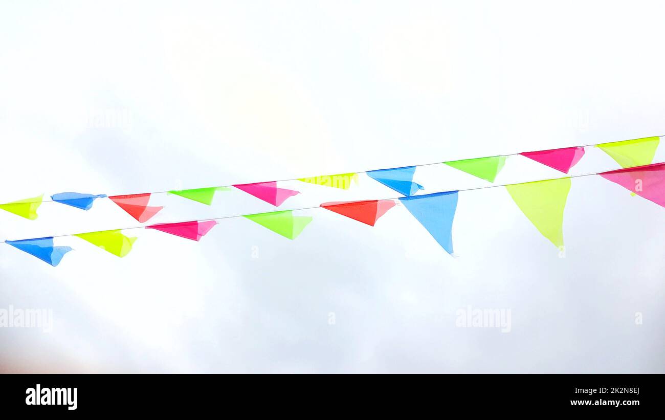 Multicolored triangular flags hang on a string and flutter in the wind against a cloudy cloudy sky Stock Photo