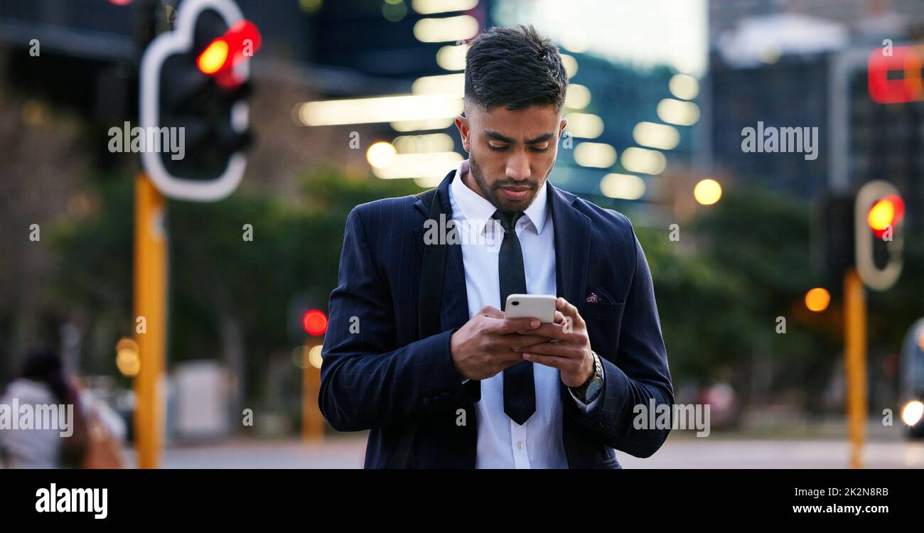 You finally received my text. Shot of a handsome young businessman walking around town using his smartphone. Stock Photo