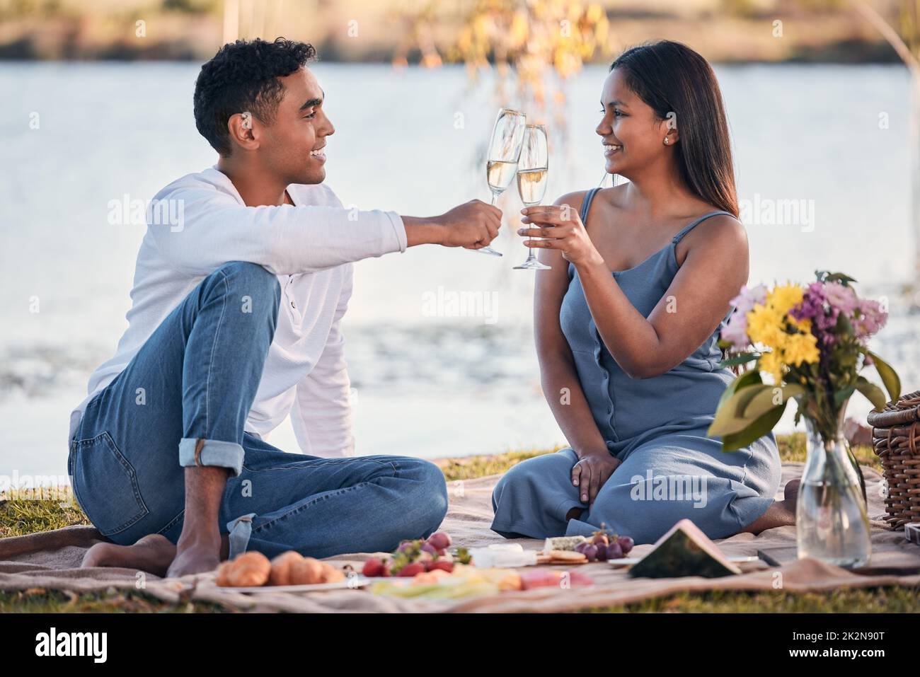 Heres to over everlasting love. Shot of a young couple making a toast while on a picnic at a lakeside. Stock Photo