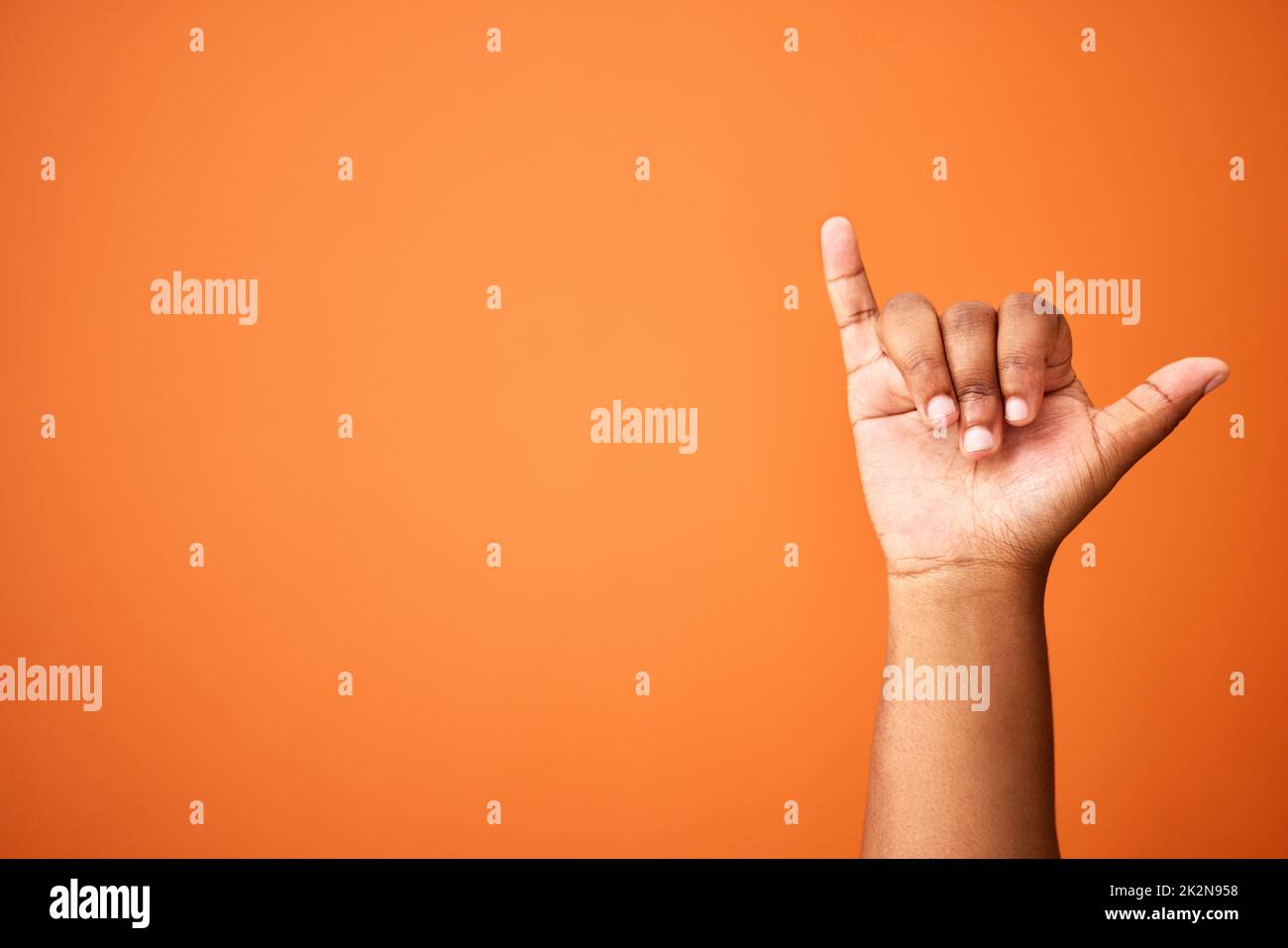 Lifes great. Shot of an unrecognizable person showing a shaka sign against an orange background. Stock Photo