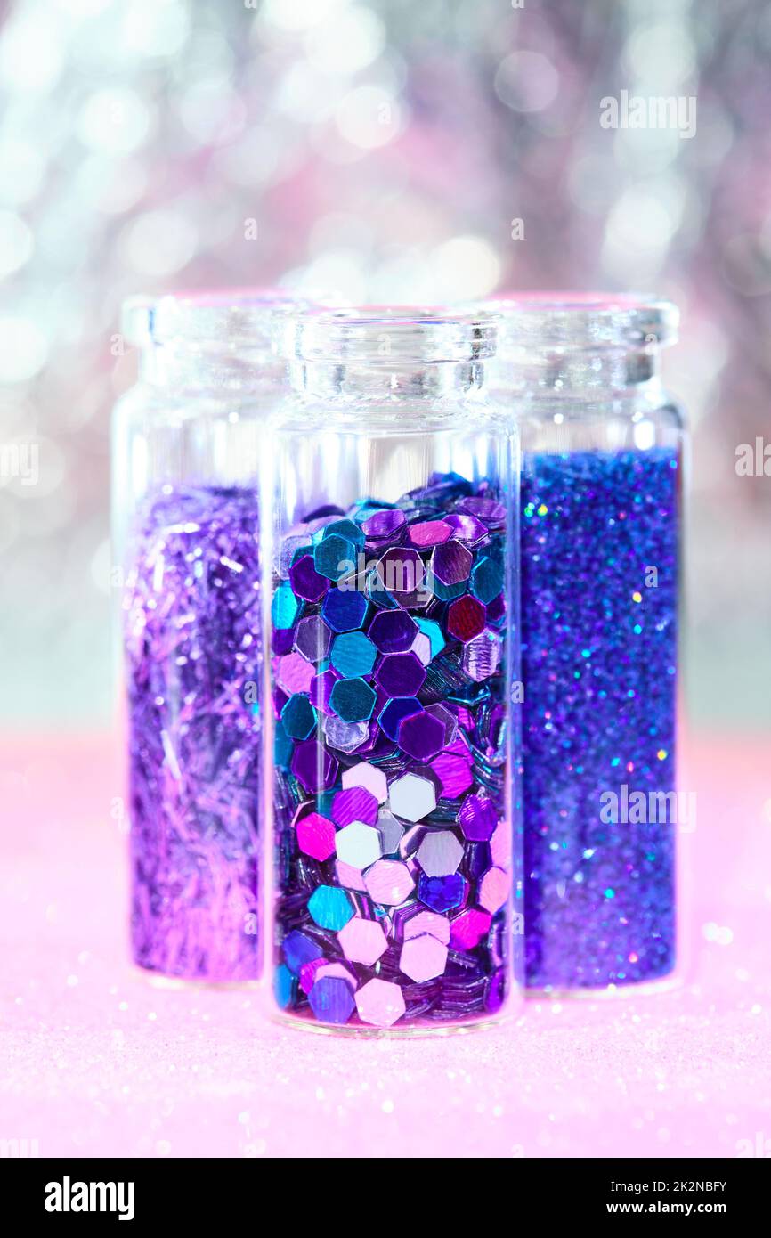All kinds of glitter products on pink sparkling background. Close-up on vials, bottles with various glitter makeup in neon pink, blue and turquoise sh Stock Photo