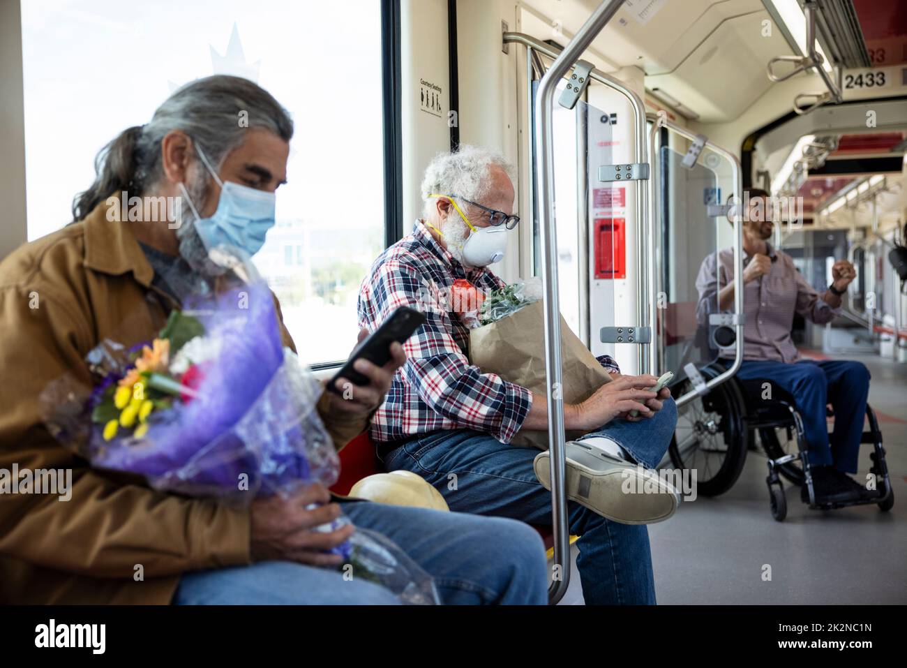 Senior male passengers in face masks using smart phones on commuter train Stock Photo